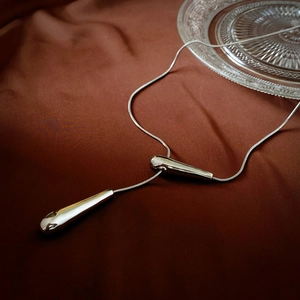 Close-up of dual silver teardrop pendants on a thin snake chain over silk fabric