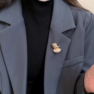 Détail d'une broche cheval à bascule dorée épinglée sur le revers d'un tailleur gris