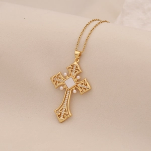 Detail view of a gold cross necklace featuring a white shell inlay and faux pearl accents