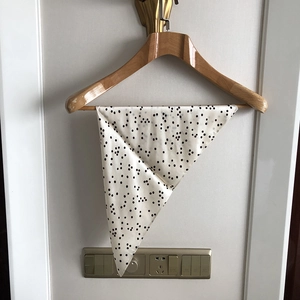 Detail of silk scarf with black polka dots on beige background hanging on wooden hanger
