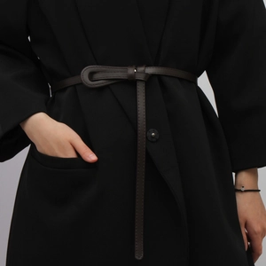 Slim dark brown leather waist belt with knot buckle styled on a black coat for women