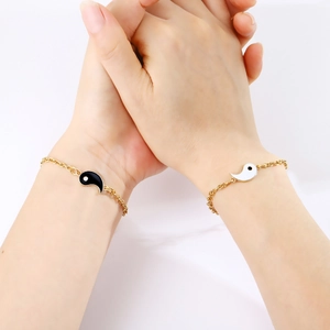 Detail view of interlocking Yin Yang charm bracelets on a couple holding hands