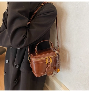 Detail of vintage brown leather bucket bag with gold hardware worn on black coat
