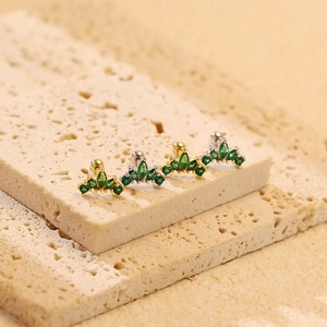 Macro shot of crown stud earrings with green cubic zirconia in silver and gold finishes
