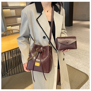 Dettaglio di una borsa a secchiello bordeaux e pochette con eleganti catene dorate