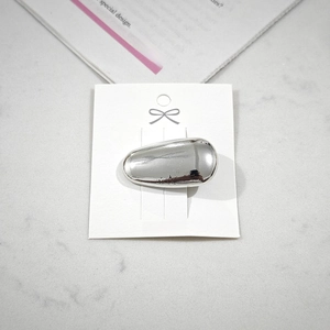 Close-up of a silver-toned oval metal hair clip on a white display card holder