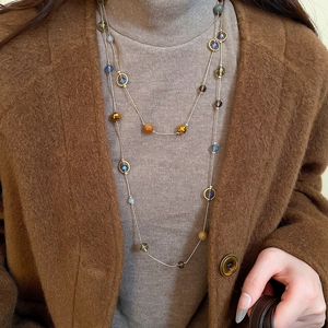 Detail einer Perlenkette mit bernsteinfarbenen Glasperlen und blauen Steinen auf Pullover