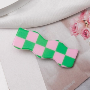 Detail of wavy green and pink checkered resin hair clip on a floral pattern background
