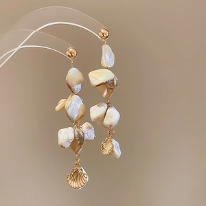 Detail of irregular shell tassel earrings with gold pendants on a clear display stand
