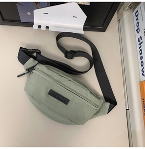 Flat lay of bean green crossbody chest bag with adjustable black strap and buckle