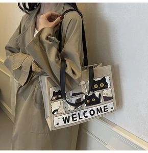 Detail of beige canvas cat tote bag shown with khaki trench coat in lifestyle setting