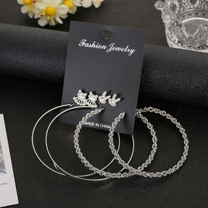 Detail view of silver metal earring set featuring rhinestones and woven hoops on a black display