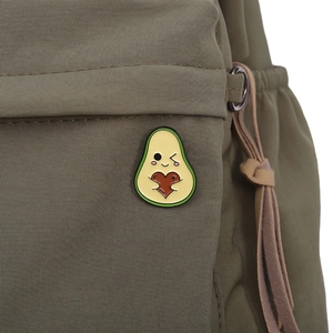 Detail showing a cartoon avocado enamel pin with a red heart on a green fabric bag