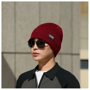 Detail of dark red ribbed knit beanie with brand patch worn with outdoor casual attire