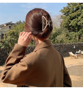Detail of a large gold metal triangle hair claw clip with pearls worn on brown hair