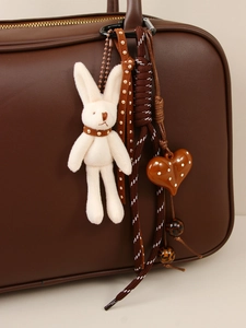 Detail of white plush rabbit charm with heart beads on a brown leather handbag zipper