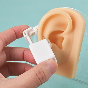 Macro shot of disposable ear piercer used on silicone ear model with white plastic tool
