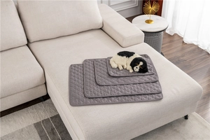 Stack of dark grey water-resistant quilted pet bed mats in four sizes on a white sofa