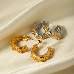 Close-up of C-shaped hoop earrings with flower relief on beige satin background