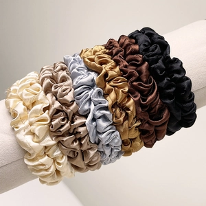 Close-up of six premium satin silk scrunchies in assorted neutral colors on a display