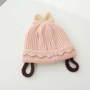 Détail d'un bonnet tricoté rose pour bébé avec nœud beige et nattes tressées mignonnes