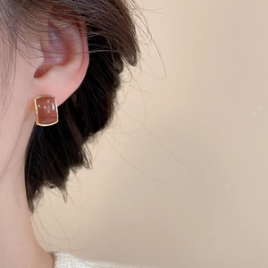 Detail view of square caramel resin earrings with gold metal base worn by model