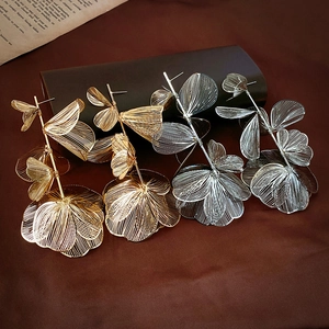 Macro detail of gold and silver wire-woven leaf earrings on a vintage paper backdrop