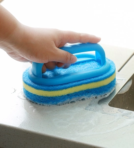 Close-up of handheld scrubbing sponge cleaning a soapy countertop with ergonomic blue handle