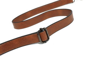 Detail of adjustable brown leather shoulder strap with dark metallic buckle on a tote bag