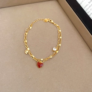 Close-up of double-layer gold bracelet with red heart and zircon stone charms