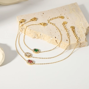 Three gold stainless steel bracelets with emerald, white, and red zircon centerpieces