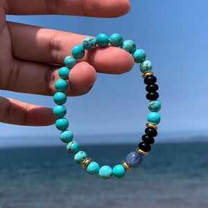 Detail of turquoise and black onyx beaded bracelet with gold spacers held by hand