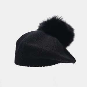 Close-up of black knitted beret hat featuring a large soft faux fur pompom on top