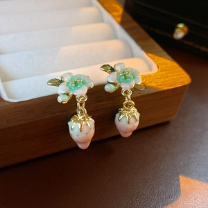 Elegant strawberry and leaf dangle earrings with enamel flowers on a wooden jewelry box