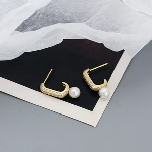 Detail of gold C-shaped earrings with white pearls and sparkling clear crystals