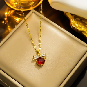 Elegant gold titanium steel necklace with a red gemstone bow pendant on a jewelry box
