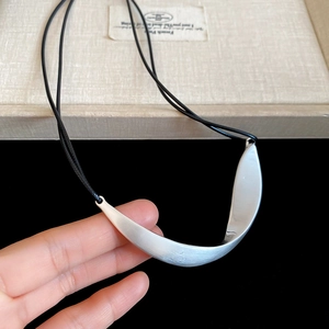 Macro detail of irregular matte silver curved pendant with brushed metal texture and black cord