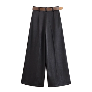 Détail du pantalon large en satin noir avec une ceinture en cuir marron sur fond blanc