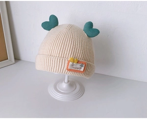 Detailed rib-knit texture of a beige baby hat with green heart accents and patch