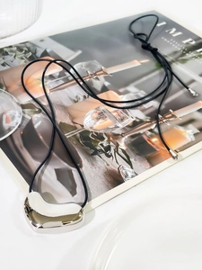 Detailed view of polished silver organic heart pendant with elegant black cord on a magazine
