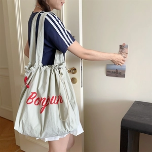 Detail of light green drawstring tote bag with red Bonjour embroidery on front