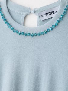 Detail of light blue knit sweater featuring sparkling rhinestone neckline and back button