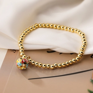 Macro detail of gold beaded bracelet featuring a colorful enamel evil eye sphere pendant