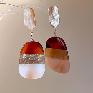 Close-up of tortoiseshell and pink acetate oval drop earrings with silver pins