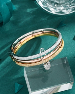 Detailed view of three-tone bangle set with pave crystals and safety pin charm accent