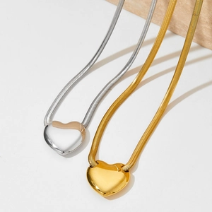 Gold and silver hollow heart necklaces with polished snake chains on stone background