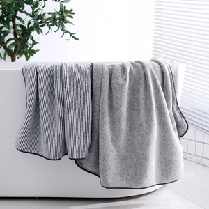 Bamboo charcoal fiber bath towels in striped grey draped over a white bathtub