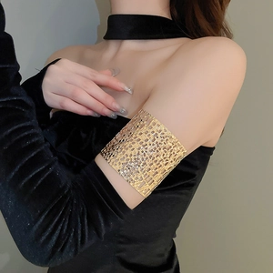 Close-up of golden hollow woven armlet worn over a black velvet evening gown sleeve