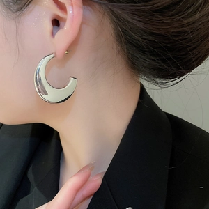 Close-up of polished silver C-shaped chunky hoop earring worn with a black suit