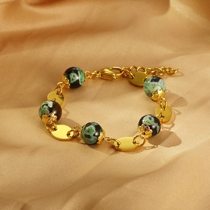 Detail of gold beaded bracelet with green and black resin beads on champagne silk
